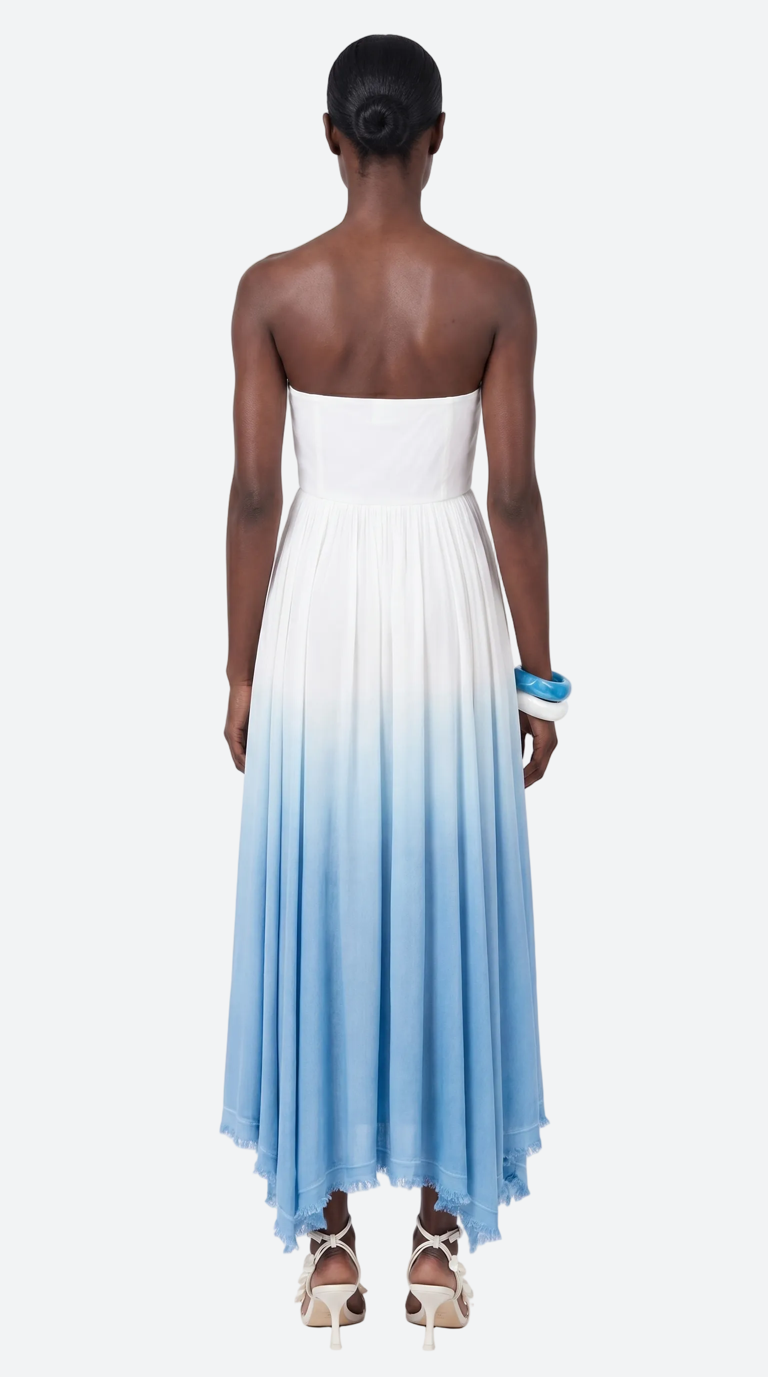 Woman wearing a evil eye crochet elexiay strapless dress with a gradient from white to blue on a white background