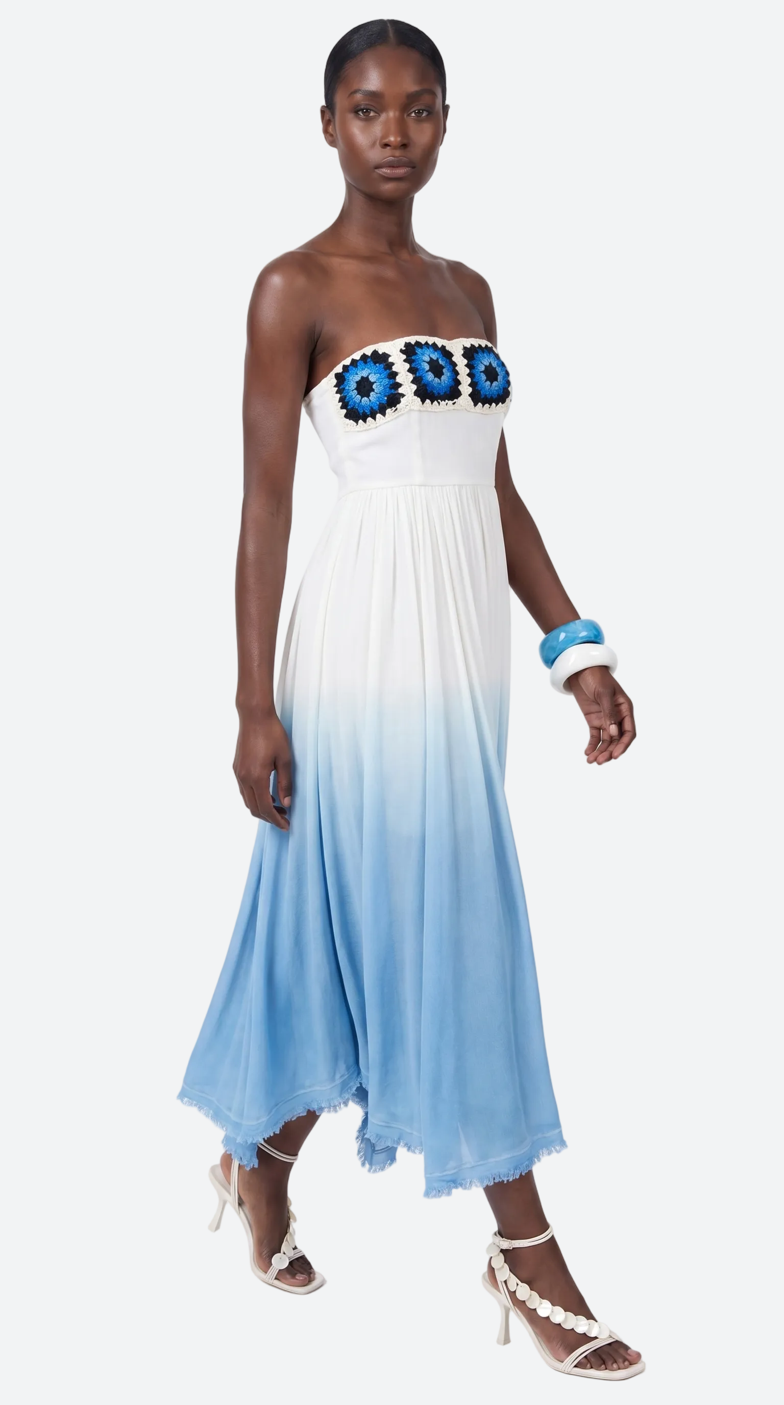 Woman wearing a strapless dress with blue floral granny square elexiay details on a white background