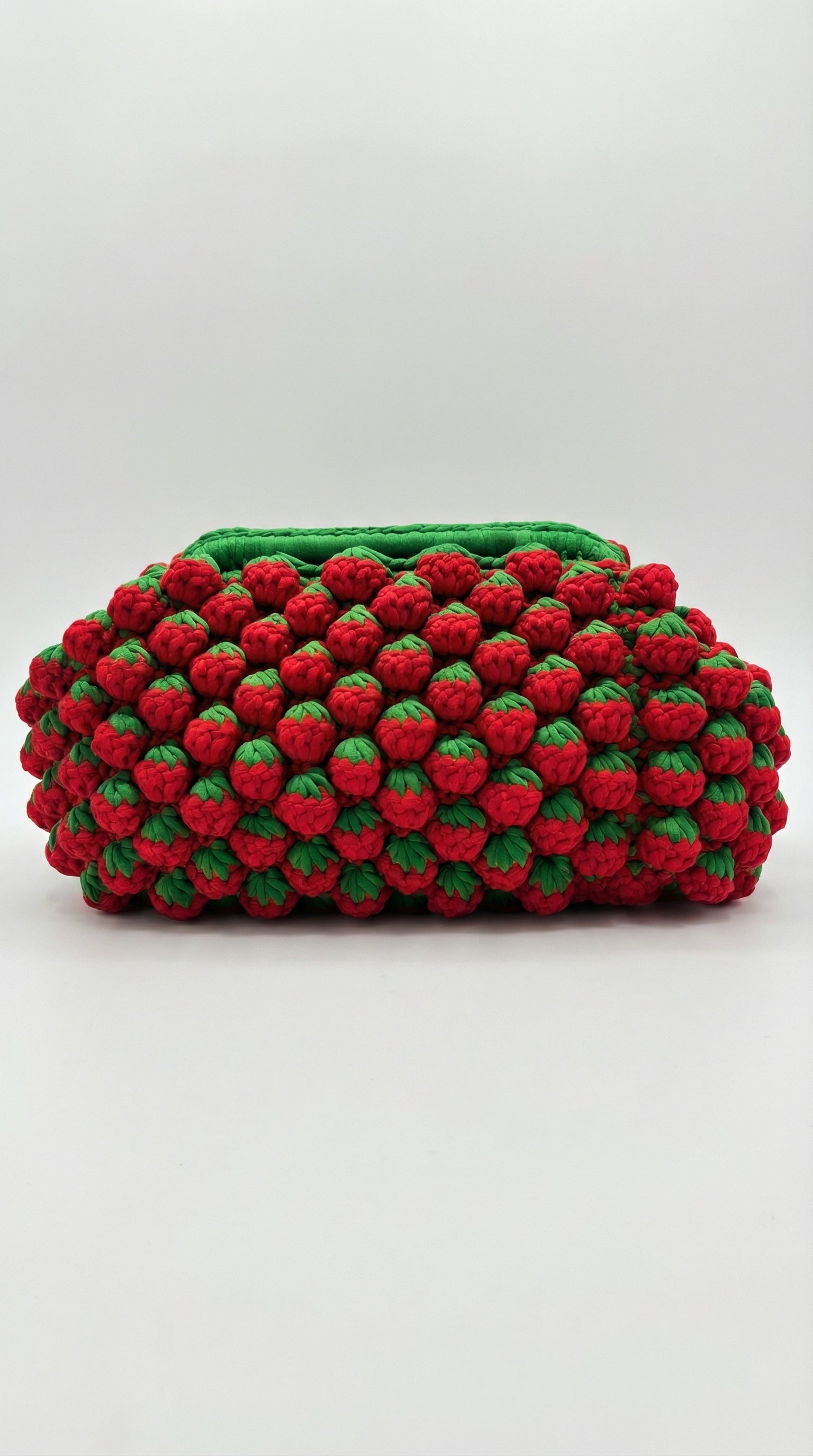 Handmade strawberry crochet clutch bag with 3D red bobble texture and green leaf detailing, side view
