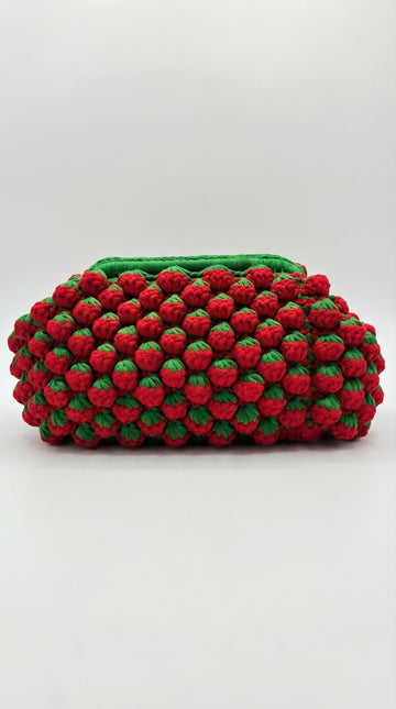 Handmade strawberry crochet clutch bag with 3D red bobble texture and green leaf detailing, side view
